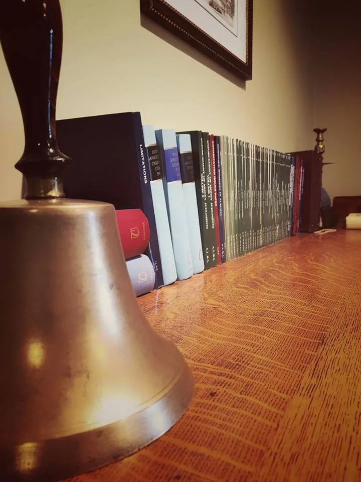 A brass bell resting on the oak table beside a row of Alberta statute books.